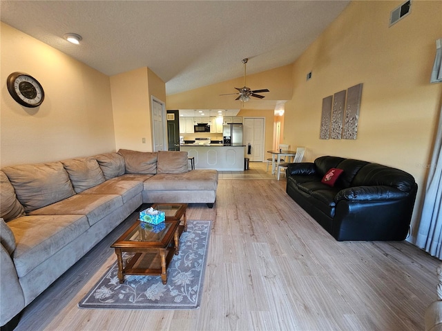 living room featuring ceiling fan, light hardwood / wood-style floors, a textured ceiling, and vaulted ceiling