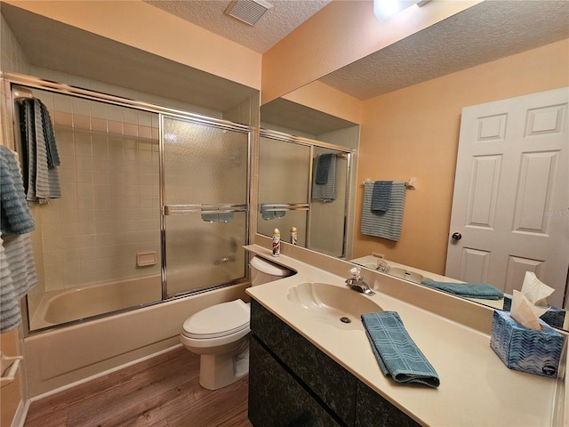 full bathroom with combined bath / shower with glass door, vanity, a textured ceiling, hardwood / wood-style flooring, and toilet