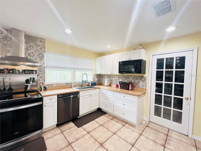 kitchen with white cabinetry, sink, wall chimney range hood, light tile patterned flooring, and black appliances