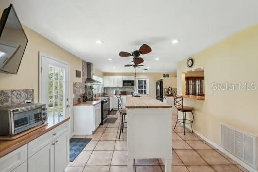 7941 Sycamore Dr, New Port Richey, FL 34654 - kitchen featuring wall chimney exhaust hood, ceiling fan, white cabinetry, a center island, and recessed lighting