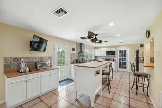 7941 Sycamore Dr, New Port Richey, FL 34654 - kitchen featuring black microwave, tasteful backsplash, ceiling fan, white cabinetry, and wall chimney exhaust hood