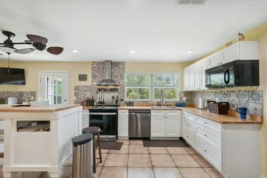 7941 Sycamore Dr, New Port Richey, FL 34654 - kitchen with wall chimney range hood, stainless steel dishwasher, range with electric stovetop, black microwave, and tasteful backsplash