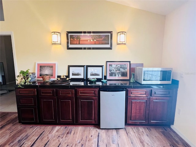 7941 Sycamore Dr, New Port Richey, FL 34654 - kitchen featuring stainless steel microwave, refrigerator, light wood-style floors, and dark countertops
