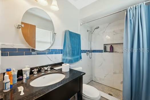 7941 Sycamore Dr, New Port Richey, FL 34654 - bathroom with a stall shower, vanity, tile walls, and decorative backsplash