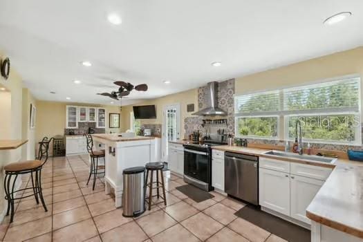 7941 Sycamore Dr, New Port Richey, FL 34654 - kitchen featuring appliances with stainless steel finishes, wall chimney range hood, a kitchen breakfast bar, recessed lighting, and white cabinets