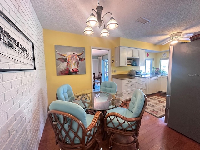 dining area with a textured ceiling, ceiling fan with notable chandelier, dark hardwood / wood-style floors, and brick wall