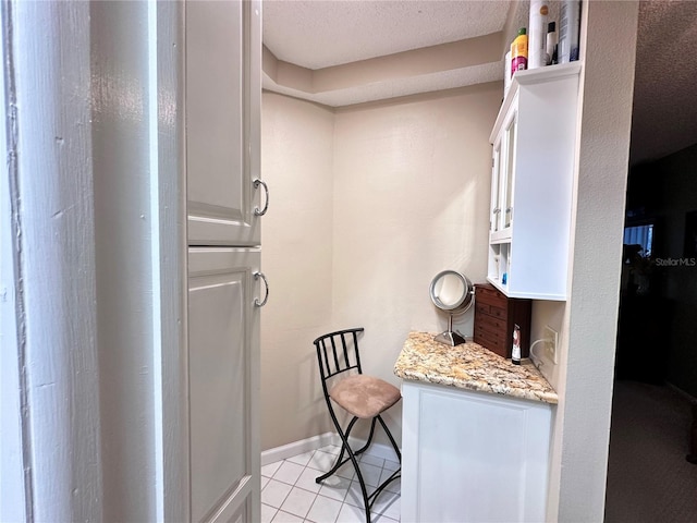 interior space featuring light stone countertops, light tile patterned floors, a textured ceiling, and white cabinetry