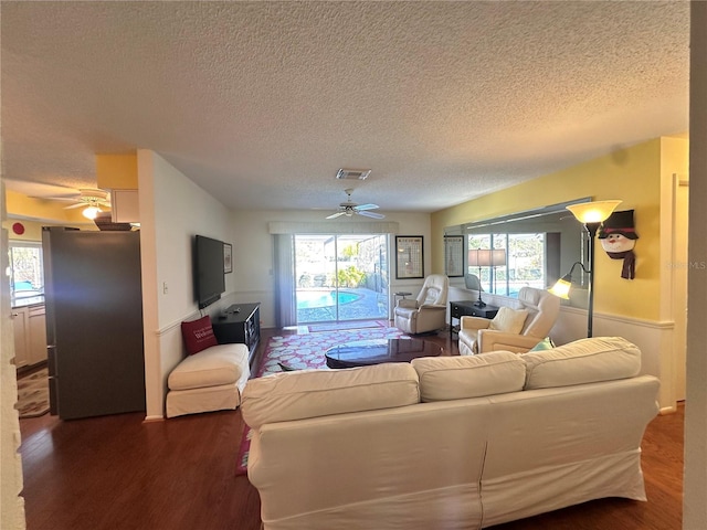 living room with a textured ceiling, ceiling fan, a healthy amount of sunlight, and dark wood-type flooring