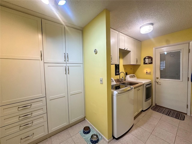 clothes washing area featuring cabinets, a textured ceiling, light tile patterned flooring, and washing machine and clothes dryer