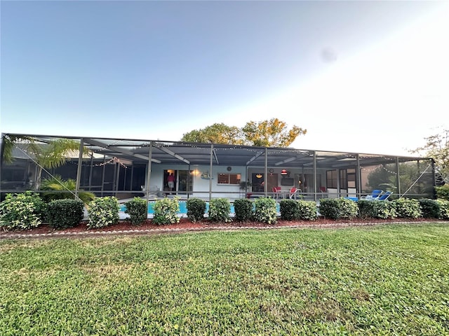 rear view of property with glass enclosure and a lawn