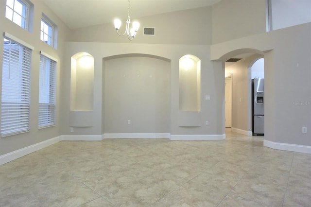 tiled spare room featuring high vaulted ceiling and a notable chandelier