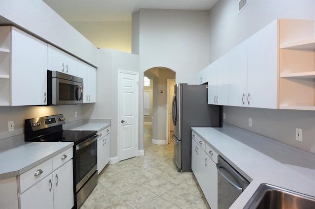 kitchen with light tile patterned floors, white cabinets, a high ceiling, and appliances with stainless steel finishes