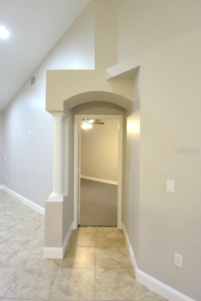 hall with decorative columns, light tile patterned floors, and vaulted ceiling