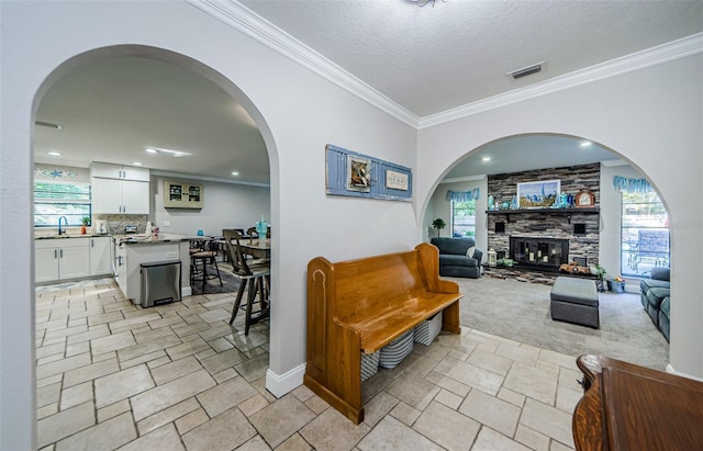 carpeted living room featuring sink, a stone fireplace, crown molding, and a textured ceiling