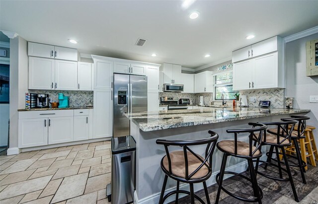 kitchen with white cabinetry, stainless steel appliances, kitchen peninsula, a breakfast bar, and ornamental molding