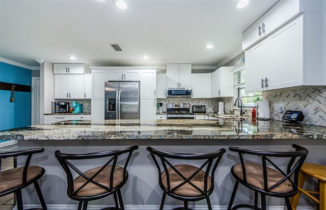 kitchen with a kitchen bar, white cabinetry, and appliances with stainless steel finishes