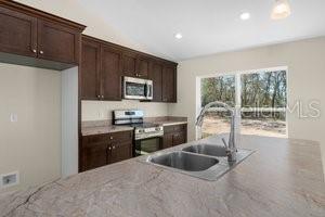 kitchen featuring light stone countertops, sink, stainless steel appliances, and dark brown cabinets