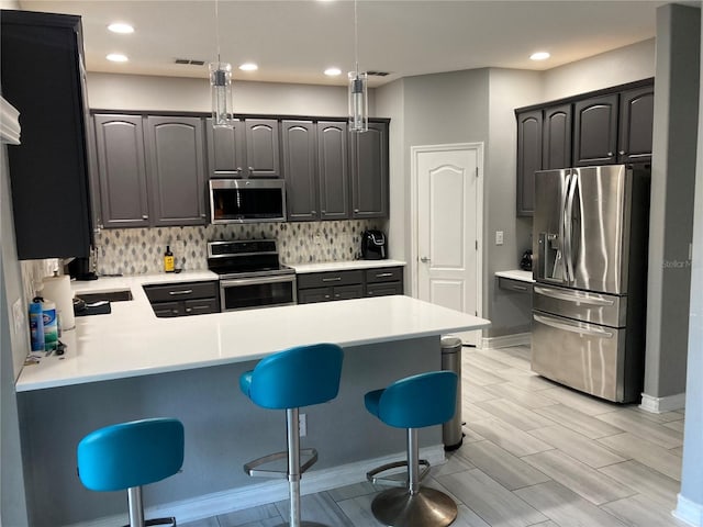 kitchen featuring kitchen peninsula, a kitchen bar, decorative backsplash, stainless steel appliances, and pendant lighting