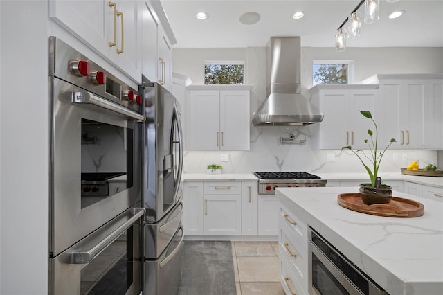 kitchen featuring light tile patterned flooring, appliances with stainless steel finishes, white cabinetry, and wall chimney range hood