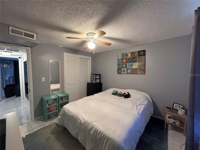 bedroom featuring ceiling fan, a closet, light tile patterned flooring, and a textured ceiling