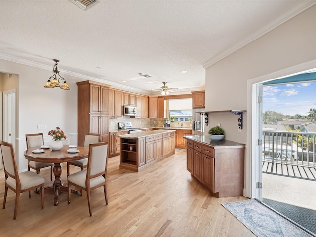 kitchen featuring appliances with stainless steel finishes, crown molding, decorative light fixtures, light hardwood / wood-style floors, and a kitchen island