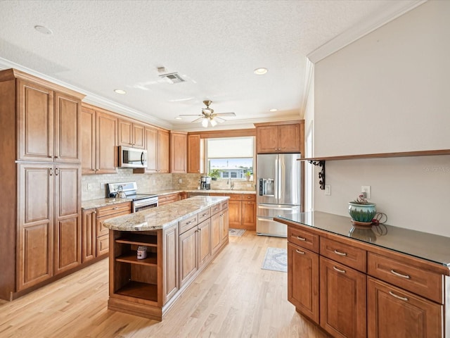 kitchen featuring a center island, stainless steel appliances, ornamental molding, a textured ceiling, and light wood-type flooring