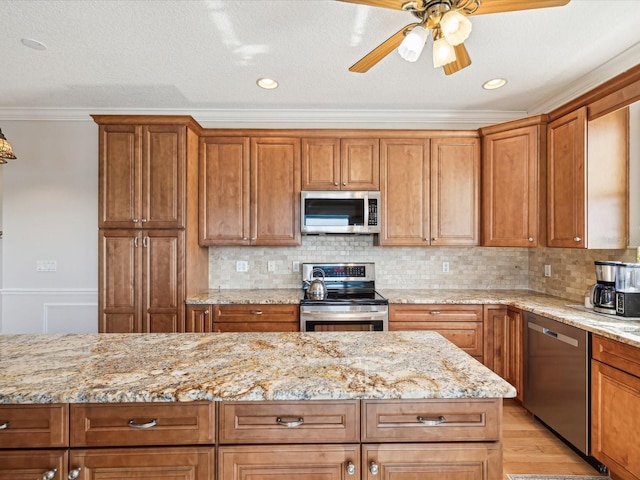 kitchen with crown molding, light hardwood / wood-style flooring, ceiling fan, light stone countertops, and appliances with stainless steel finishes