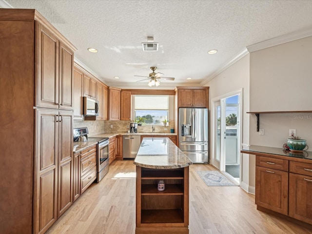 kitchen featuring ornamental molding, a kitchen island, light wood-type flooring, and appliances with stainless steel finishes