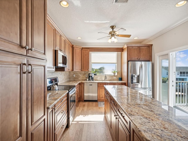 kitchen with light stone countertops, appliances with stainless steel finishes, light wood-type flooring, backsplash, and ornamental molding