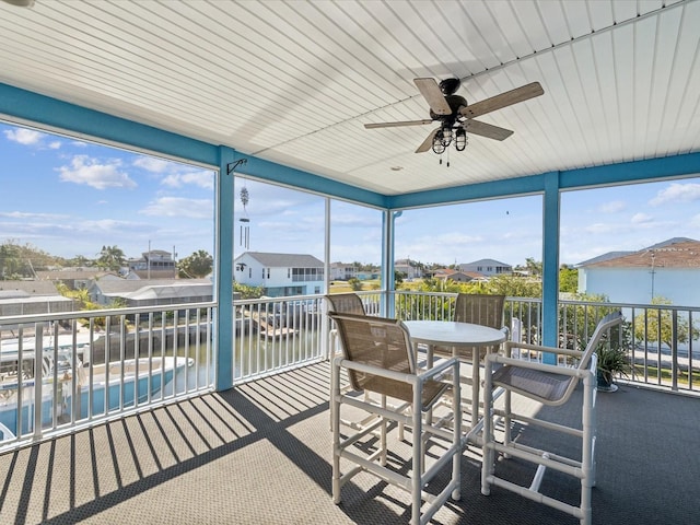 sunroom with ceiling fan and a water view