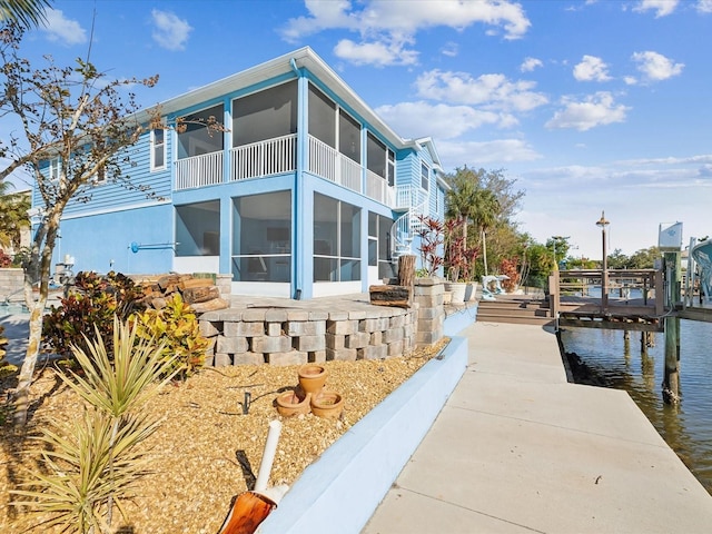 view of side of property with a water view, a sunroom, and a dock