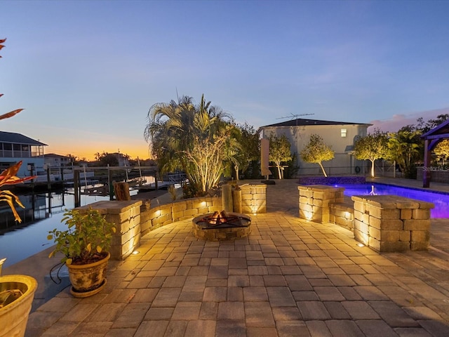 patio terrace at dusk featuring a gazebo, a fire pit, a water view, and pool water feature