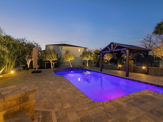 pool at dusk featuring a gazebo and a patio area