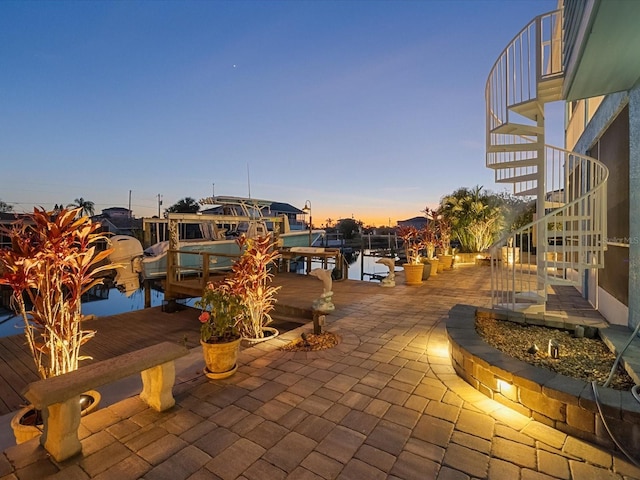 patio terrace at dusk featuring a dock and a water view