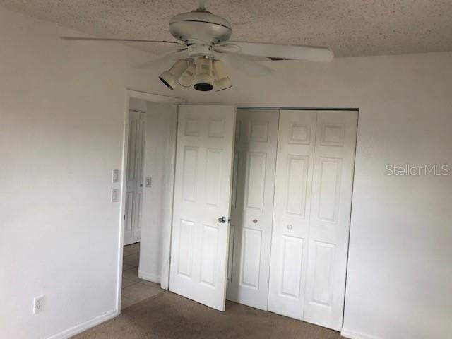 unfurnished bedroom featuring dark colored carpet, a textured ceiling, a closet, and ceiling fan