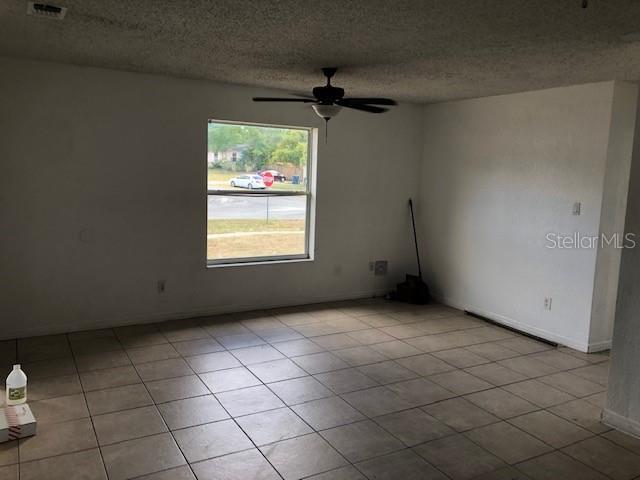 spare room featuring ceiling fan, light tile patterned floors, and a textured ceiling