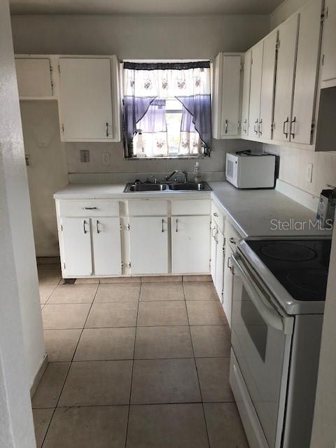 kitchen featuring white cabinetry, sink, light tile patterned floors, and white appliances