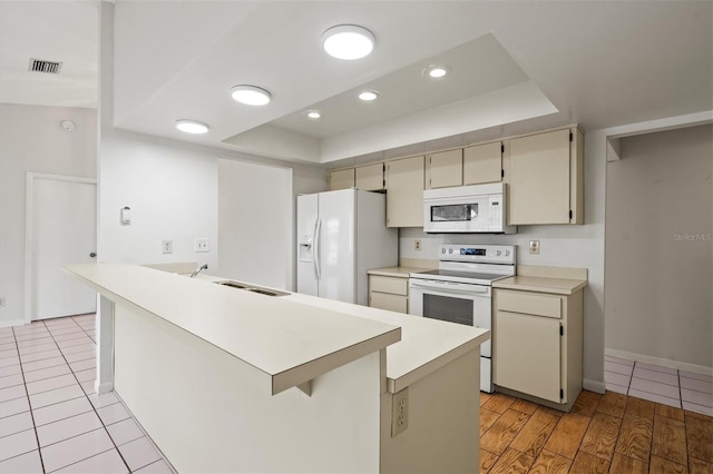 kitchen with sink, a breakfast bar area, kitchen peninsula, white appliances, and cream cabinetry