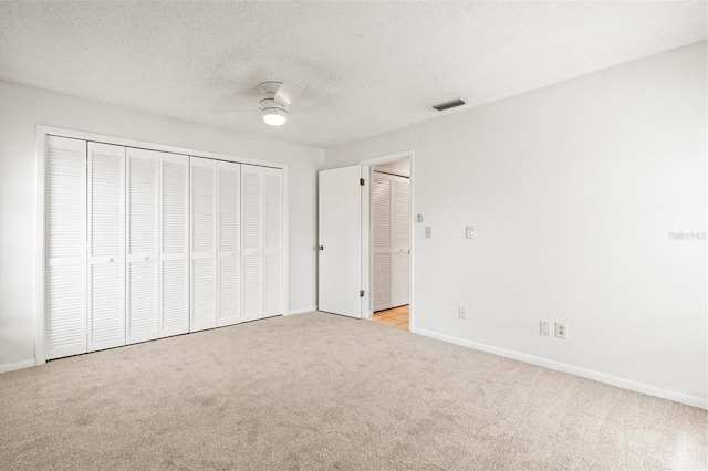 unfurnished bedroom featuring light carpet, a textured ceiling, ceiling fan, and a closet