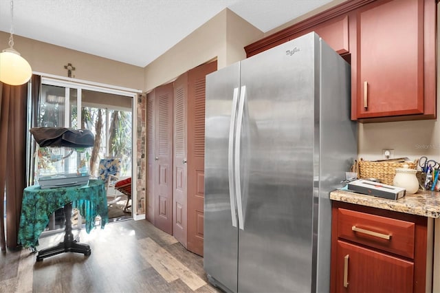 kitchen featuring hanging light fixtures, light hardwood / wood-style flooring, light stone countertops, a textured ceiling, and stainless steel refrigerator