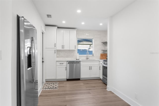 kitchen featuring appliances with stainless steel finishes, tasteful backsplash, sink, white cabinets, and light hardwood / wood-style floors