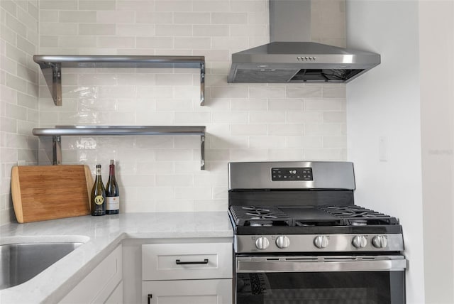 kitchen with stainless steel range with gas cooktop, tasteful backsplash, white cabinets, light stone countertops, and wall chimney range hood