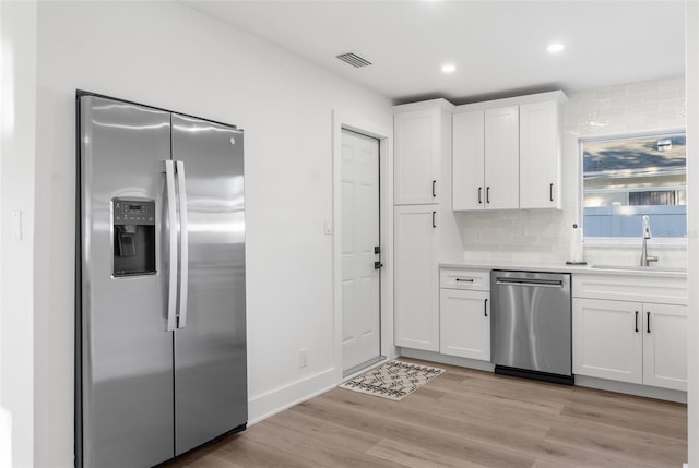 kitchen featuring sink, light hardwood / wood-style flooring, stainless steel appliances, tasteful backsplash, and white cabinets