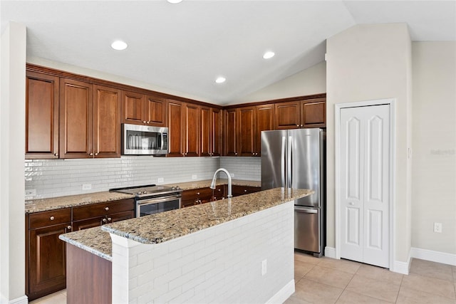 kitchen with appliances with stainless steel finishes, decorative backsplash, an island with sink, light stone counters, and lofted ceiling