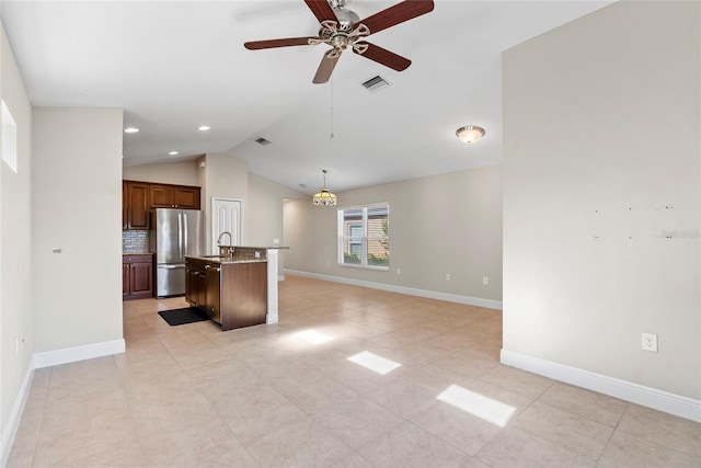 kitchen featuring tasteful backsplash, stainless steel fridge, pendant lighting, a center island with sink, and lofted ceiling