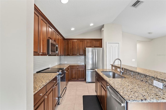 kitchen featuring sink, light stone counters, an island with sink, lofted ceiling, and stainless steel appliances