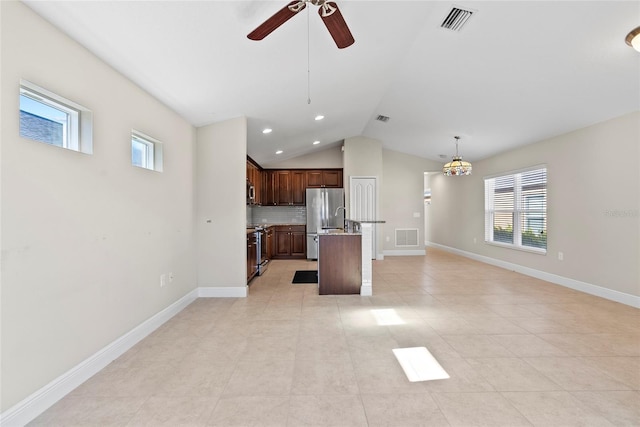 kitchen with appliances with stainless steel finishes, a kitchen island with sink, decorative backsplash, pendant lighting, and vaulted ceiling