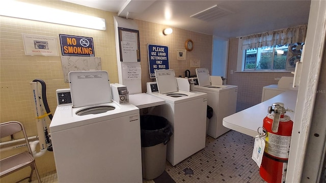 washroom featuring light tile patterned flooring, washing machine and dryer, and tile walls