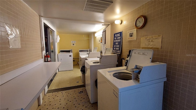 laundry area with separate washer and dryer, light tile patterned floors, and tile walls