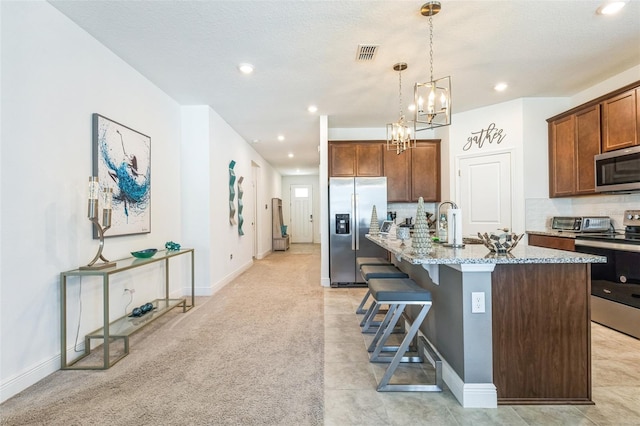 kitchen with light stone countertops, a kitchen breakfast bar, stainless steel appliances, pendant lighting, and a center island with sink